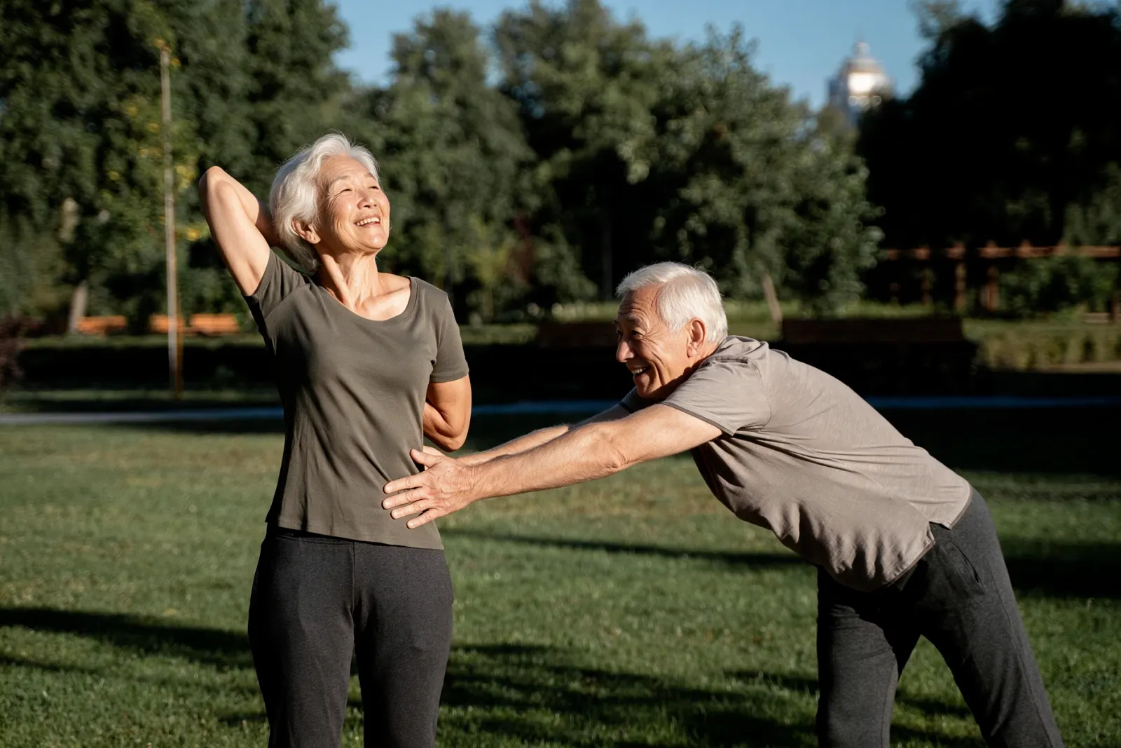 An older couple stretching together on a sunny lawn