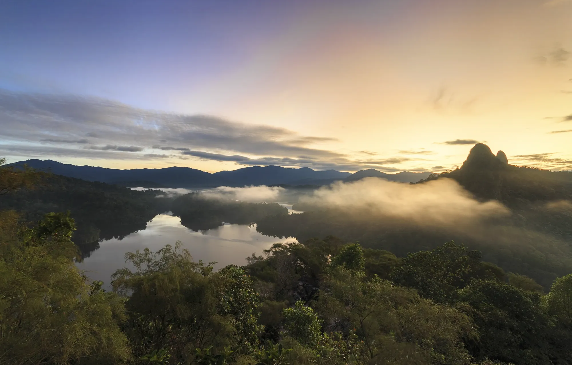 A forested valley at sunrise, mist lying over a lake between the hills